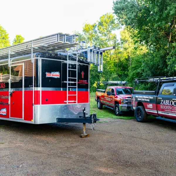 Zablocki Roofing trucks and an equipment trailer parked at a wooded Central Minnesota job site.
