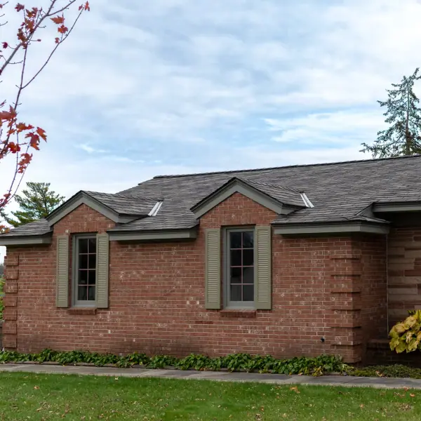 Red brick ranch home showing new brown shingles across the main roof plane and two gables.