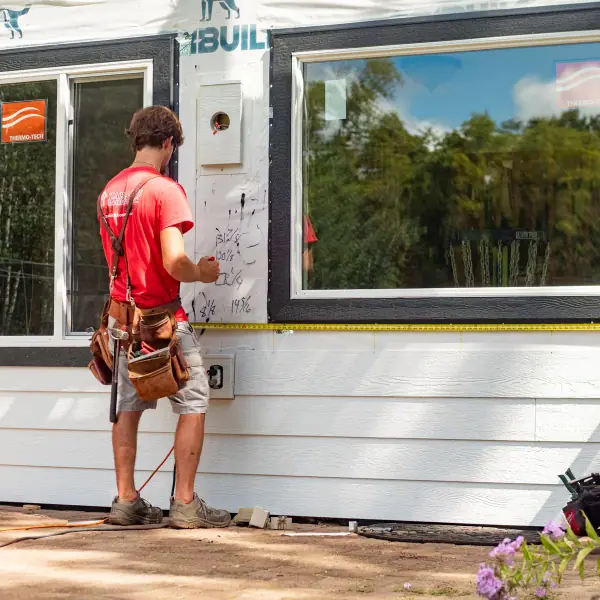 New white lap siding and black-trimmed windows as two crew members measure a window opening.