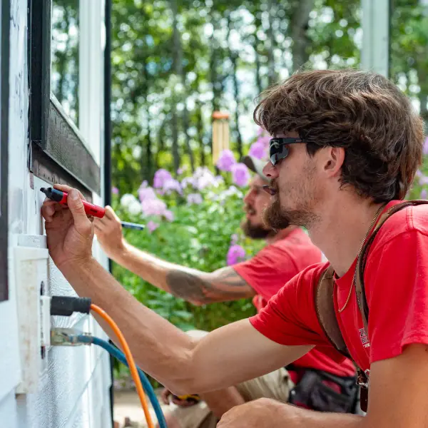 Two installers marking trim around a window opening on a partly sided Central Minnesota home.